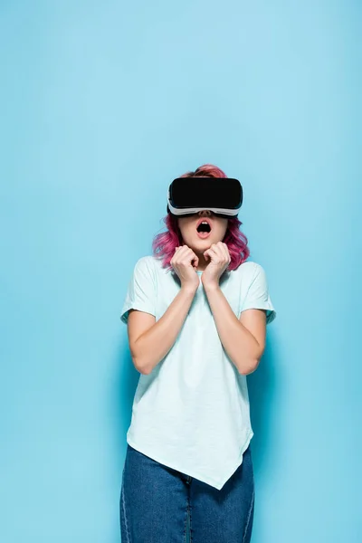 Effrayée jeune femme avec des cheveux roses en vr casque sur fond bleu — Photo de stock