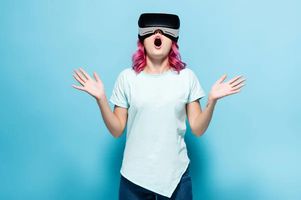 Chocado jovem mulher com cabelo rosa no vr fone de ouvido gesticulando no fundo azul — Fotografia de Stock