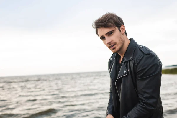 Young man in leather jacket looking at camera near sea — Stock Photo