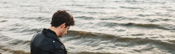 Panorâmica tiro de homem em jaqueta de couro em pé perto do mar — Fotografia de Stock