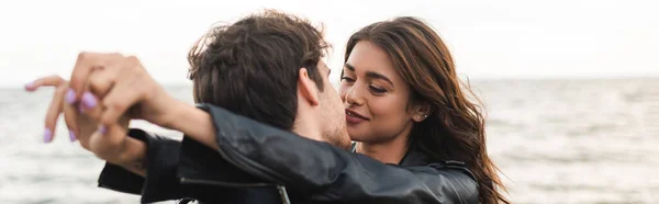 Panoramic shot of man kissing girlfriend in leather jacket near sea — Stock Photo