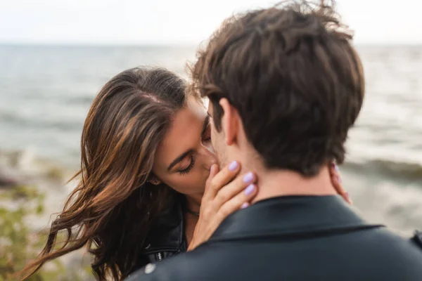 Selective focus of young woman kissing boyfriend on sea coast — Stock Photo