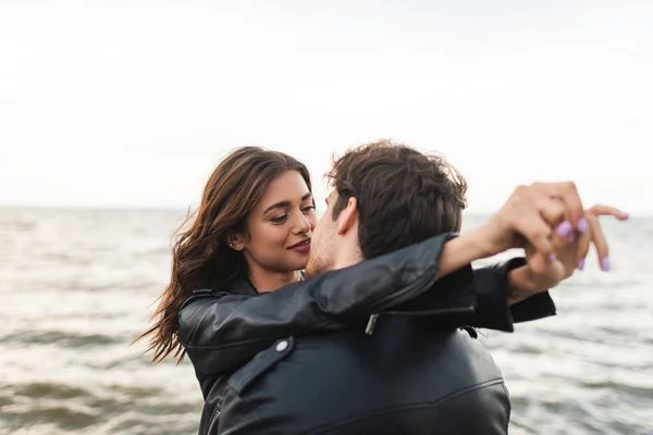 Мужчина в кожаной куртке целует женщину у моря — стоковое фото