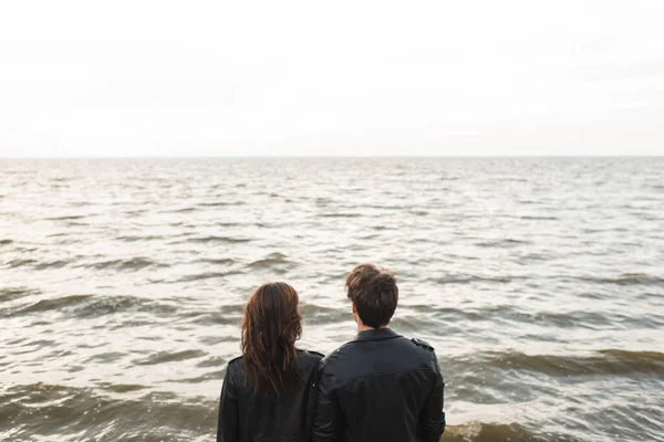 Вид ззаду пара в чорних шкіряних куртках дивиться на море — стокове фото