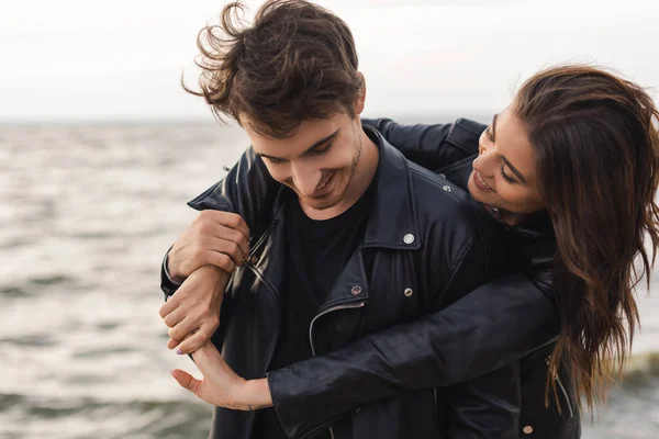 Brunette woman hugging boyfriend in leather jacket near sea — Stock Photo