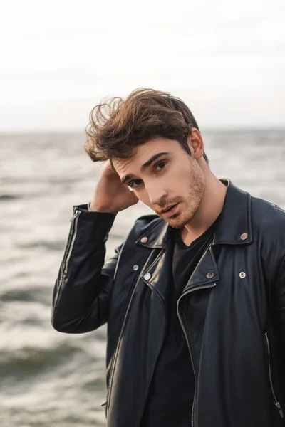 Young man in leather jacket looking at camera near sea — Stock Photo