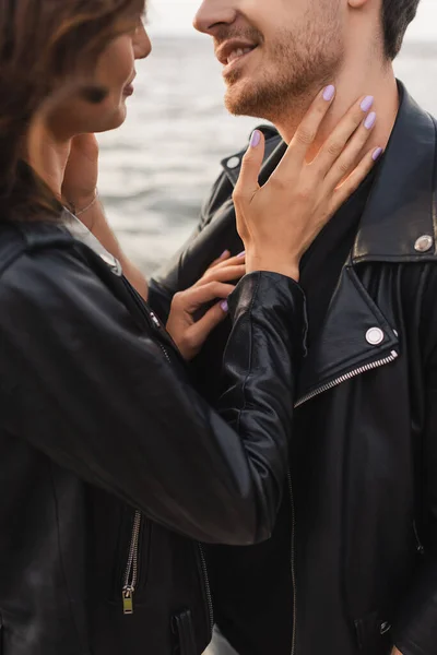 Vista recortada de mujer tocando cuello de novio en chaqueta de cuero cerca del mar - foto de stock