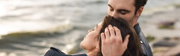 Horizontal image of young man kissing head of brunette girlfriend near sea — Stock Photo