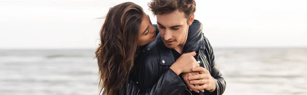 Panoramic shot of young woman embracing boyfriend in leather jacket beside sea — Stock Photo