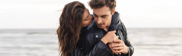 Foto panorámica de mujer joven abrazando novio en chaqueta de cuero al lado del mar - foto de stock