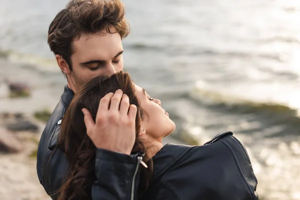 Man kissing and touching hair of woman in leather jacket on beach — Stock Photo