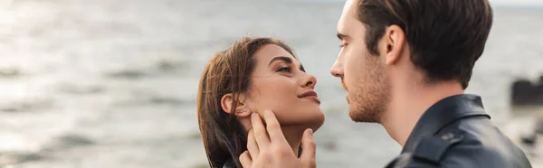 Website header of man in leather jacket touching cheek of girlfriend near sea — Stock Photo