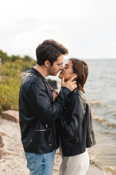 Vue latérale du couple en vestes en cuir s'embrassant sur le bord de mer — Photo de stock