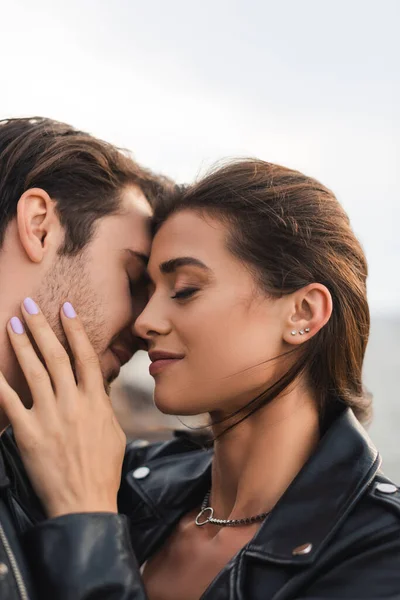 Young woman in leather jacket touching boyfriend with closed eyes outdoors — Stock Photo