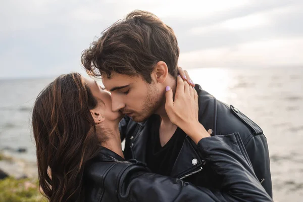 Giovane donna toccante collo del fidanzato in giacca di pelle sulla spiaggia — Foto stock