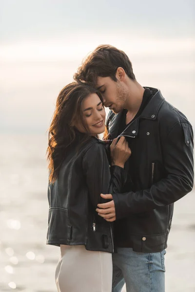 Mujer morena en vestido y chaqueta de cuero de pie cerca de novio y el mar - foto de stock