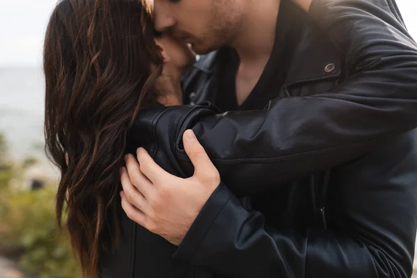 Hombre besando y abrazando morena novia en chaqueta de cuero en la playa - foto de stock