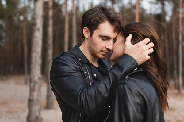 Hombre en chaqueta de cuero besando y tocando novia en el bosque - foto de stock