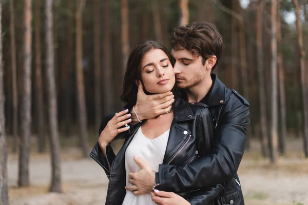 Joven tocando novia en chaqueta de cuero con los ojos cerrados en el bosque - foto de stock