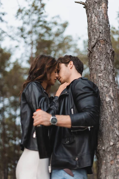 Selective focus of woman kissing boyfriend with bottle of wine near tree in forest — Stock Photo