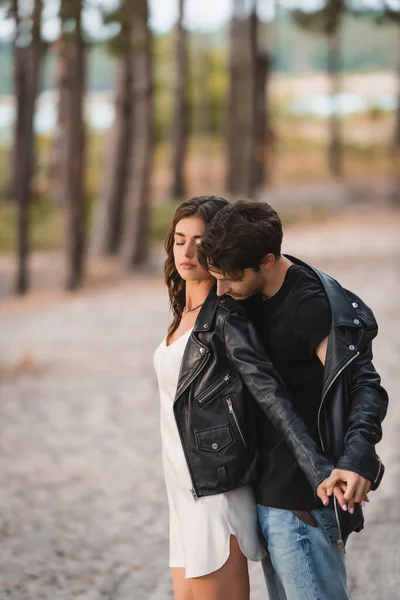 Man holding hand of brunette girlfriend in leather jacket in forest — Stock Photo