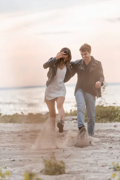 Selective focus of young couple throwing sand on sea cost at sunset — Stock Photo