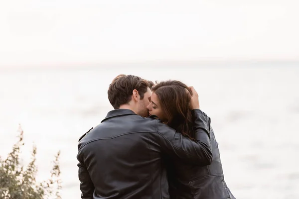 Вид ззаду молода пара в шкіряних куртках цілується біля моря — стокове фото