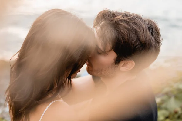 Foco seletivo do jovem beijando mulher morena perto do mar — Fotografia de Stock