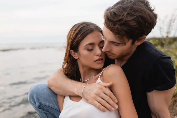 Young man embracing brunette girlfriend on seaside — Stock Photo