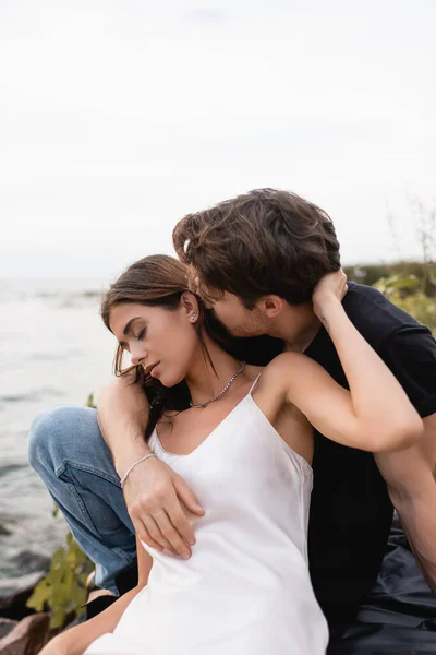 Молодой человек целует девушку в платье на пляже у моря — стоковое фото