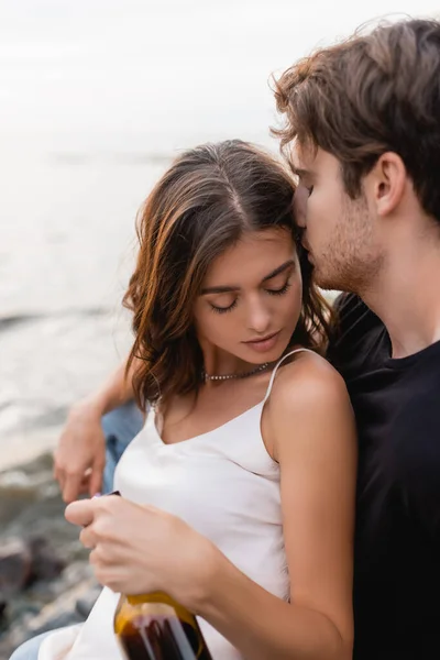 Focus selettivo del giovane baciare fidanzata con bottiglia di vino sulla spiaggia — Foto stock