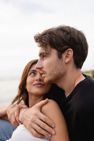 Young man hugging girlfriend and looking away on beach — Stock Photo