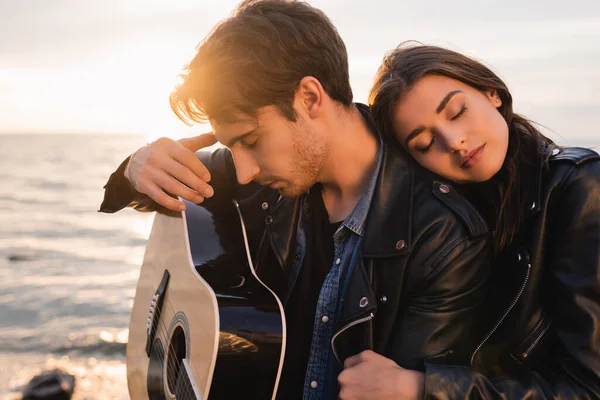Young man holding acoustic guitar near woman on beach at sunset — Stock Photo