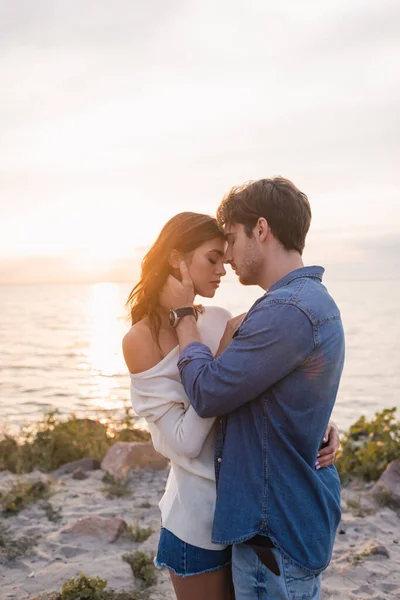 Casal jovem tocando uns aos outros e abraçando na costa do mar à noite — Fotografia de Stock