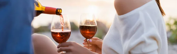 Panorâmica tiro de homem derramando vinho em copos perto da namorada na praia — Fotografia de Stock