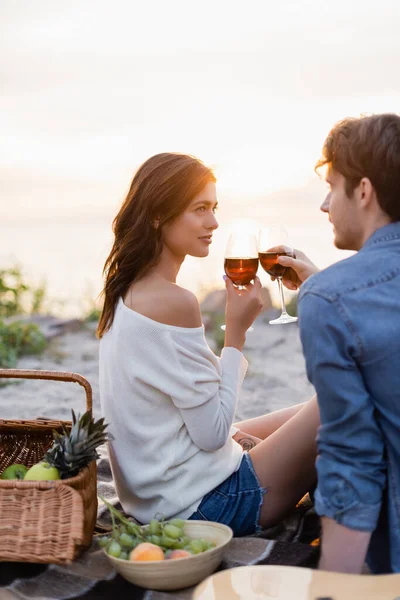 Selektiver Fokus des Paares, das beim Picknick am Strand bei Sonnenuntergang mit Wein klingelt — Stockfoto