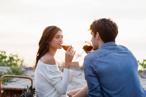 Concentration sélective de la femme buvant du vin avec son petit ami pendant le pique-nique sur la plage — Photo de stock