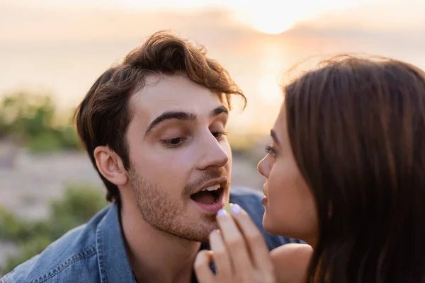 Focus selettivo della giovane donna che alimenta il fidanzato con uva sulla spiaggia al tramonto — Foto stock