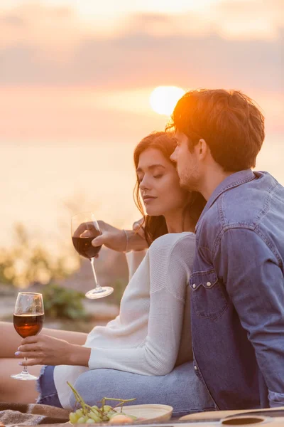 Selective focus of man embracing girlfriend with glass of wine near acoustic guitar on beach — Stock Photo