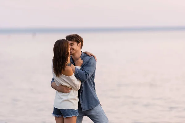 Young man kissing girlfriend near sea at evening — Stock Photo