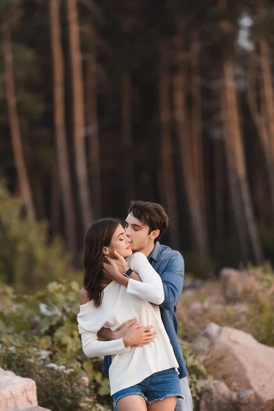 Homem beijando e abraçando jovem mulher perto da floresta — Fotografia de Stock