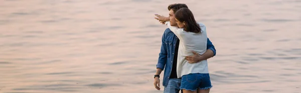 Imagem horizontal da jovem mulher abraçando namorado perto do mar ao pôr do sol — Fotografia de Stock