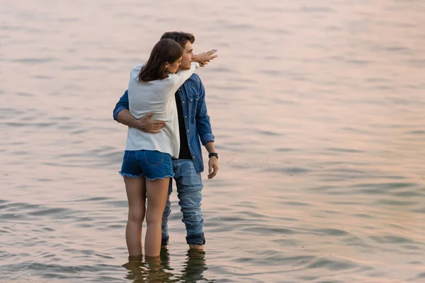 Young couple embracing while standing in water of sea at evening — Stock Photo