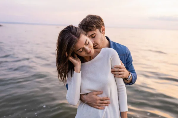 Homme embrassant cou et câlin petite amie près de la mer le soir — Photo de stock