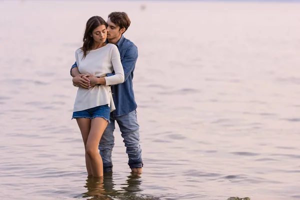 Young couple embracing while standing together in sea at evening — Stock Photo