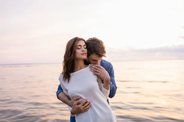 Homme touchant jeune copine près de la mer avec coucher de soleil ciel à l'arrière-plan — Photo de stock