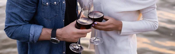 Cultura horizontal de casal segurando copos de vinho perto do mar — Fotografia de Stock