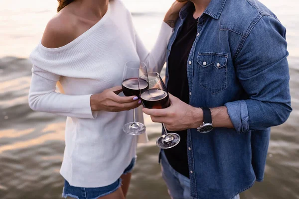 Vista cortada de jovem casal segurando copos de vinho perto do mar — Fotografia de Stock