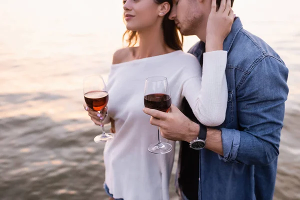Vista recortada de la mujer tocando novio mientras sostiene una copa de vino cerca del mar - foto de stock