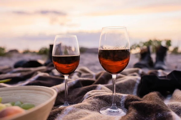 Selective focus of glasses of wine near fruits in bowl on plaid on beach — Stock Photo